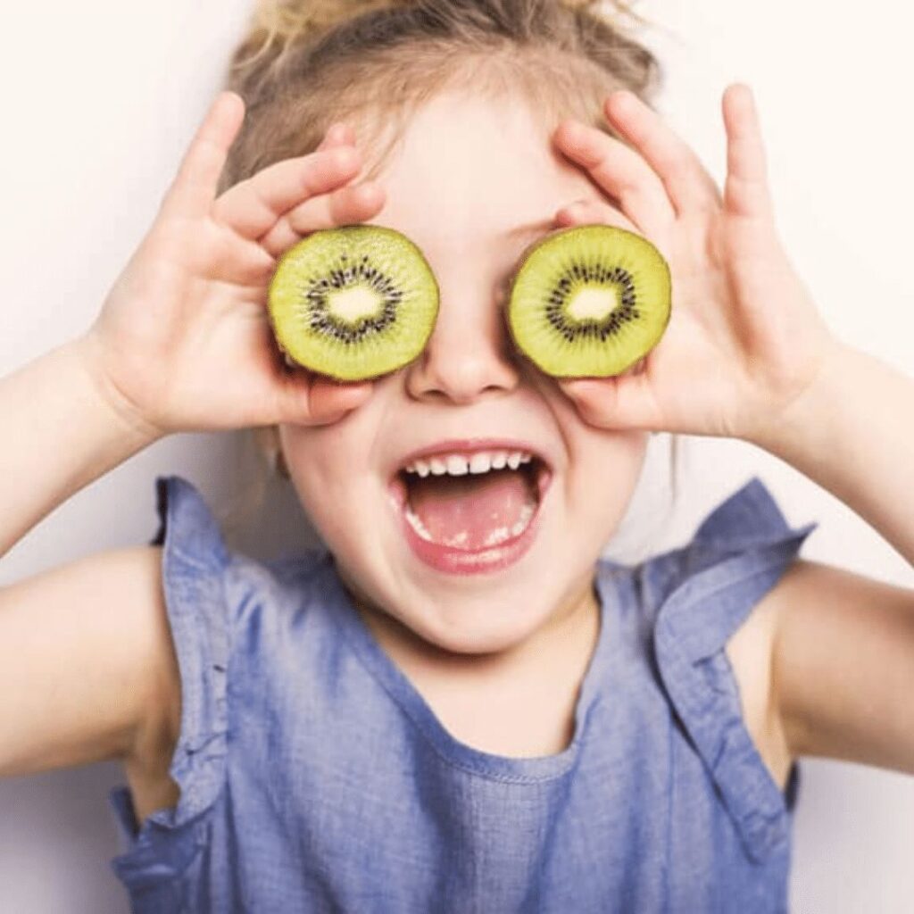 Een kind die twee halve kiwi's voor haar ogen houdt en lacht