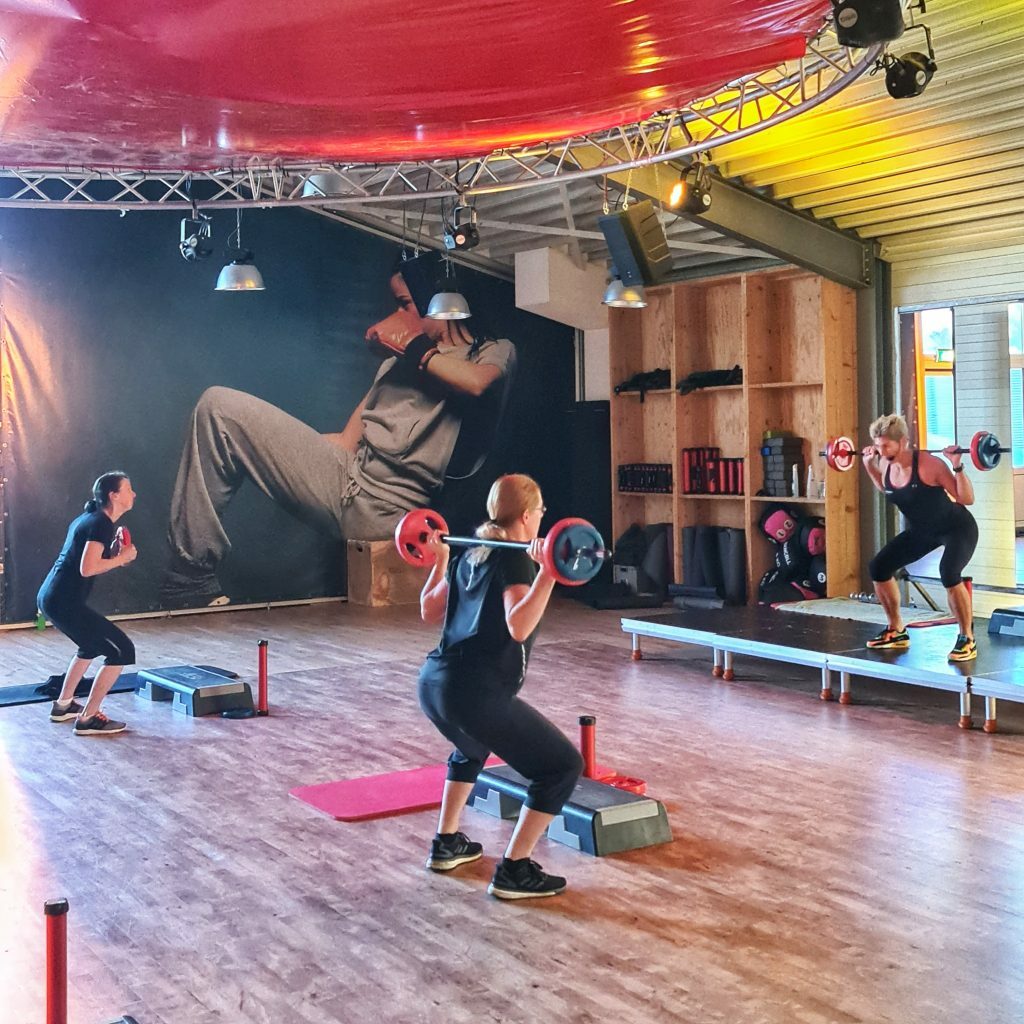 Een twee dames die gewichten heffen tijdens een groepsles onder begeleiding van een groepslesdocent.