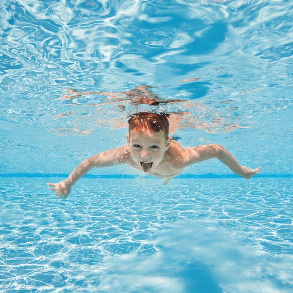 Een kind die lachend onderwater aan het zwemmen is tijdens de zwemles
